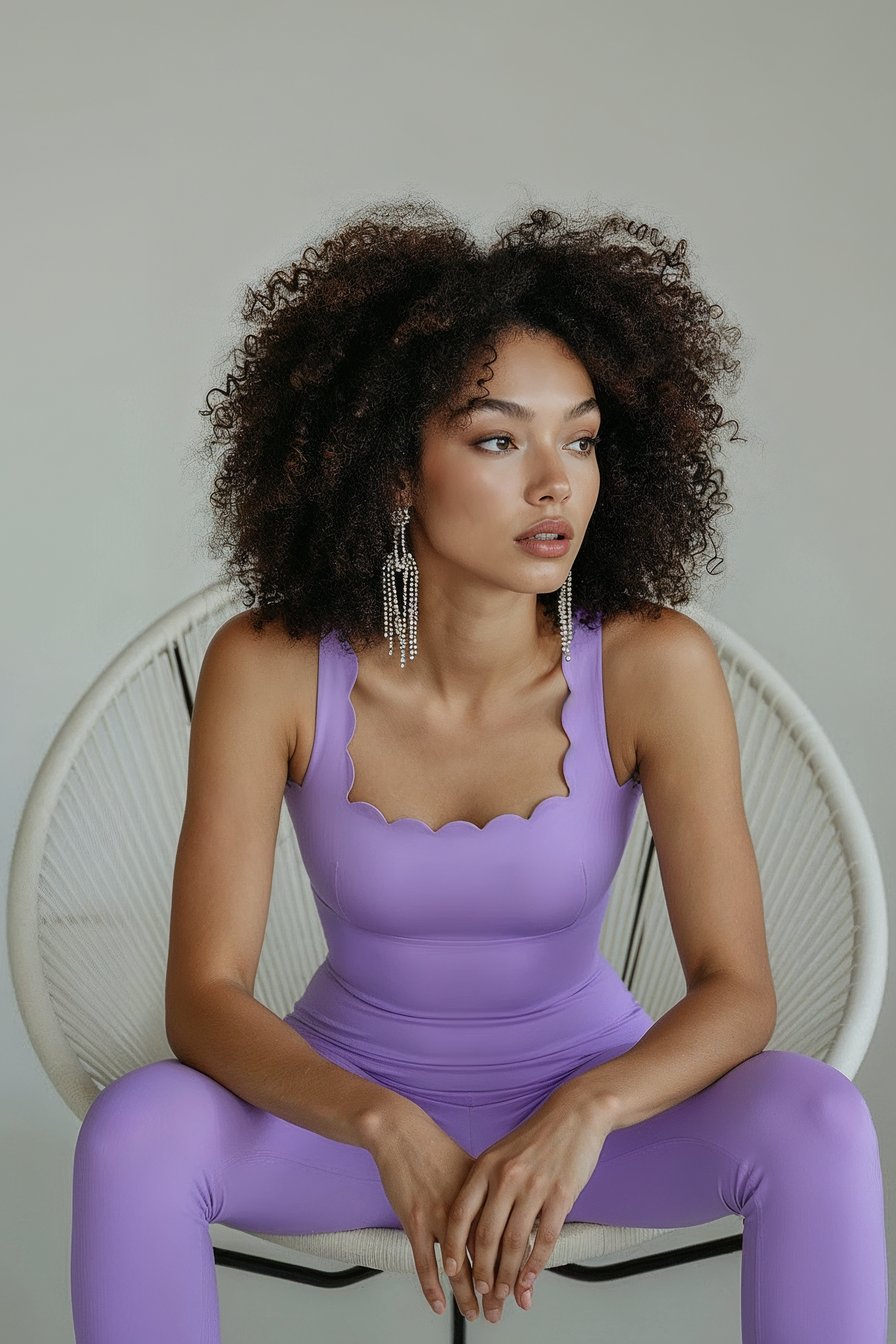 Woman in a purple outfit sitting on a white chair against a neutral background