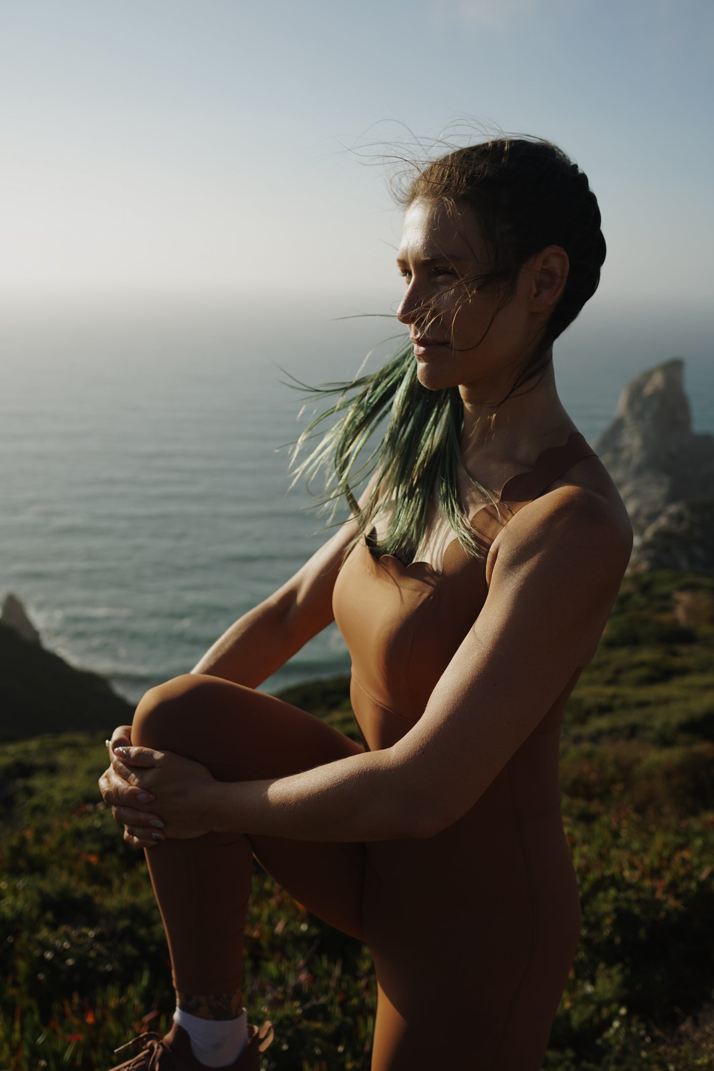 Person sitting on a cliff overlooking the ocean with mountains in the background